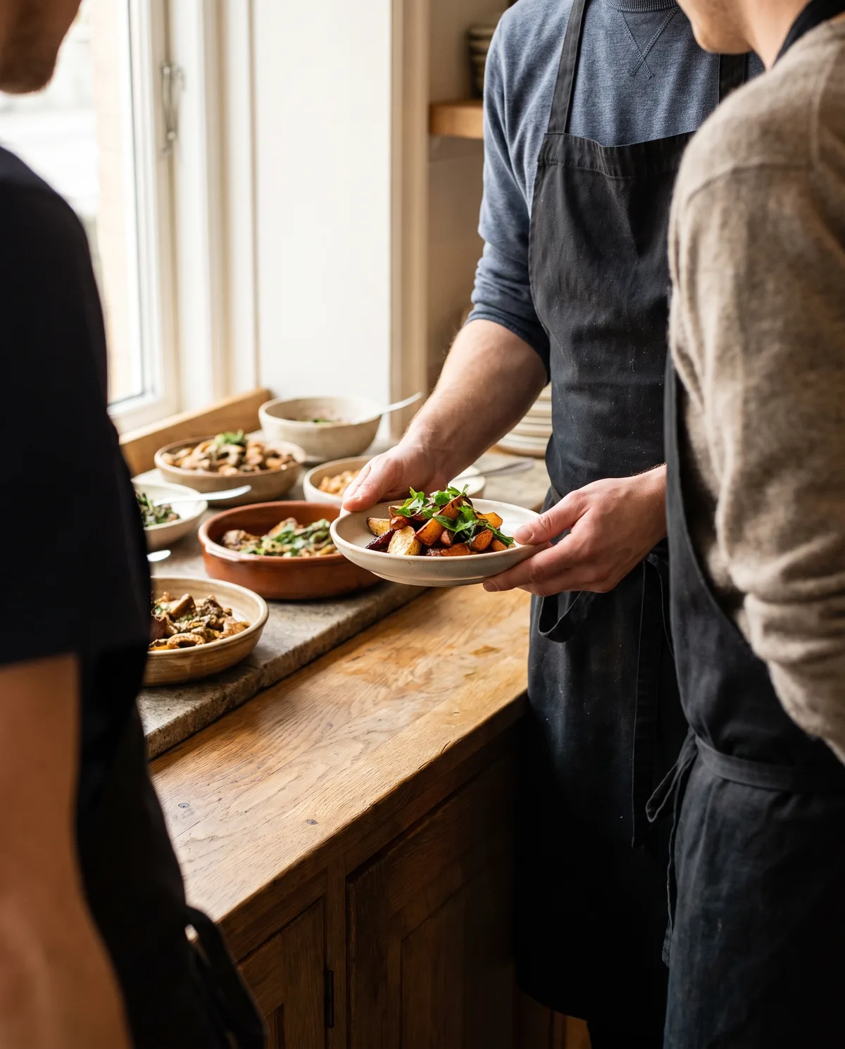 Restaurantleder og gæst i kort samtale ved buffeten, set fra siden, begge med ryggen halvt til, mad mellem dem